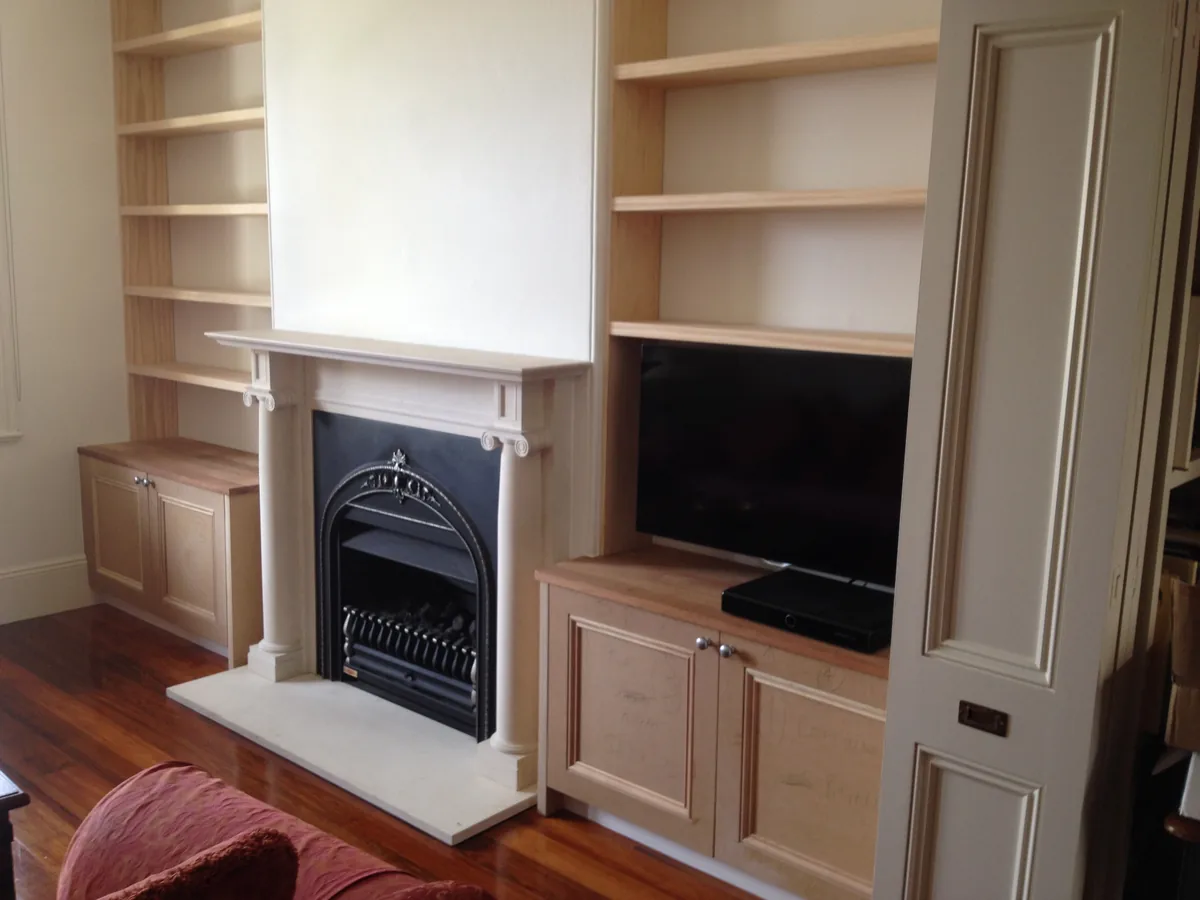 Custom white built-in cupboards and shelving beside a fireplace